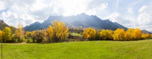 Vista panoramica de Paisaje  otoñal de prados verdes arboledas y montañas rocosas  al fondo. Con pequeño pueblo escondido entre los arboles